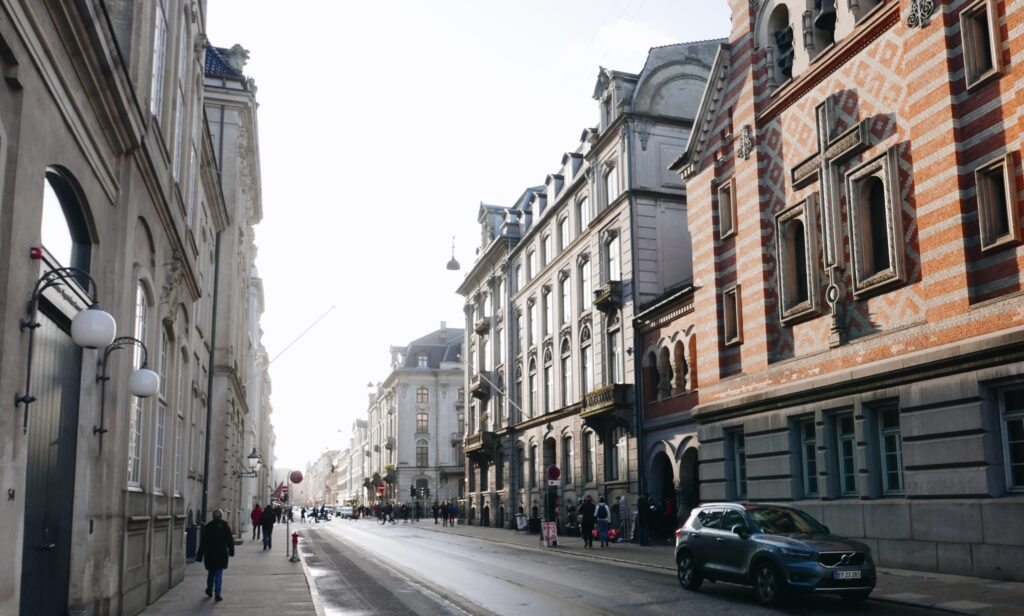 Københavnsk bygade med klassiske andelsforeningsejendomme og fodgængere på fortovet en lys dag.