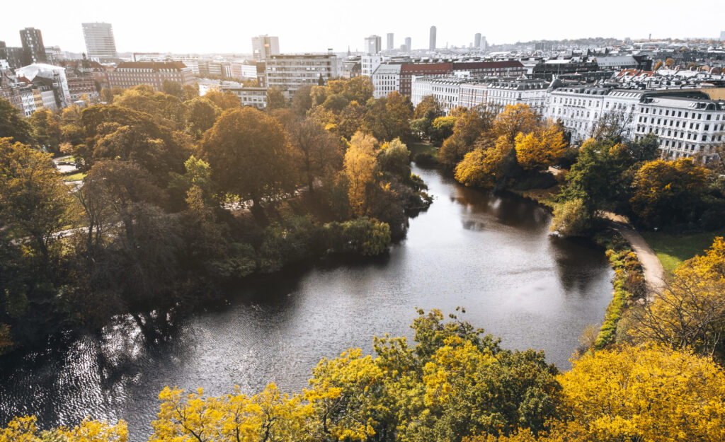 Efterårslandskab i København med sø, træer og andelslejligheder i baggrunden – set fra oven.
