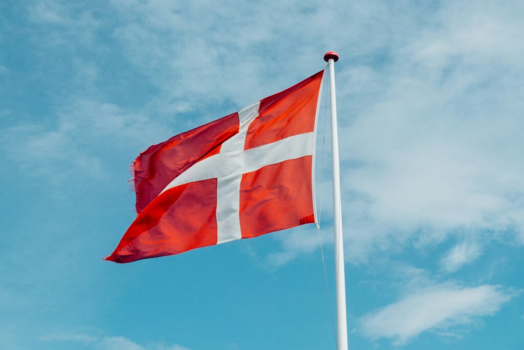 Det danske flag, Dannebrog, vajer mod blå himmel, symbol på fællesskab og ejendomsadministration